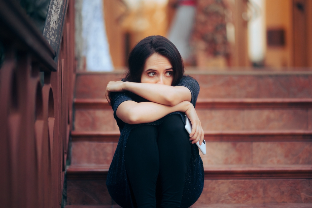 Woman sitting on the steps looking worried in an article by Caroline Maguire on how to ease anxiety when socializing.